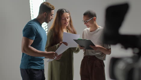 Film-Director-Talking-With-Male-And-Female-Actors-Holding-Scripts-Rehearsing-For-Shooting-Movie-Or-Video-In-Studio-2